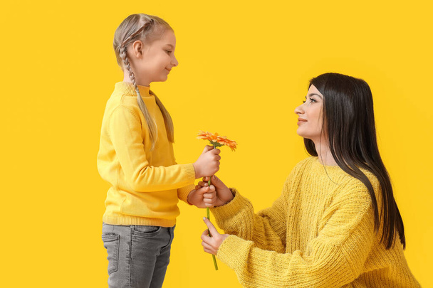 Kleines Mädchen und ihre Mutter mit Blume auf gelbem Hintergrund - Foto, Bild