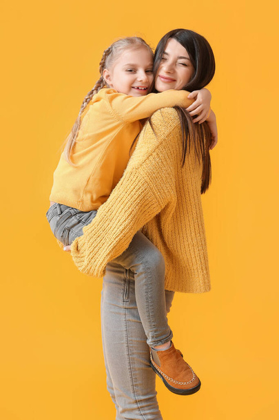 Little girl and her mother in warm sweaters on yellow background - Photo, Image