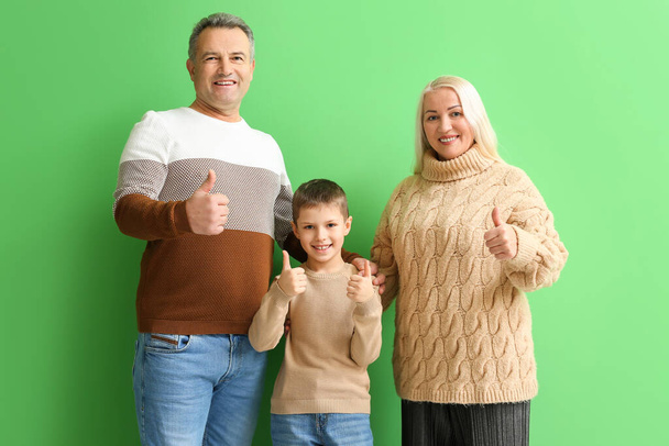 Büyük annesi ve büyük babasıyla birlikte yeşil arka planda baş parmak gösteren küçük bir çocuk. - Fotoğraf, Görsel
