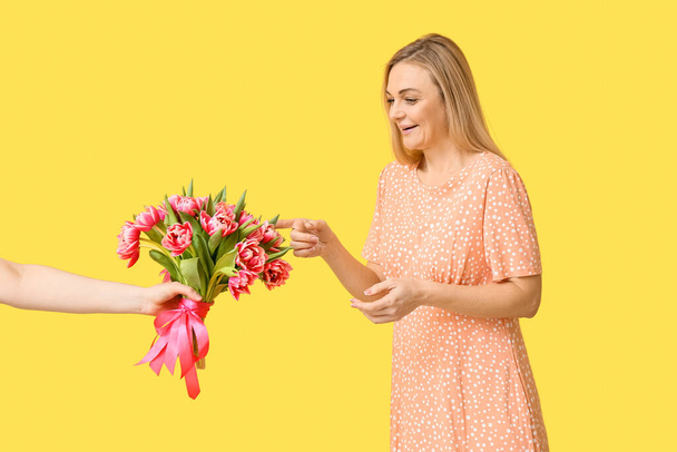 Beautiful woman receiving bouquet of flowers on yellow background. International Women's Day celebration - Foto, Imagen