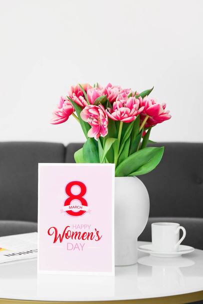 Greeting card with text HAPPY WOMEN'S DAY, vase with tulips, cup of coffee and newspaper on table in room - Foto, imagen