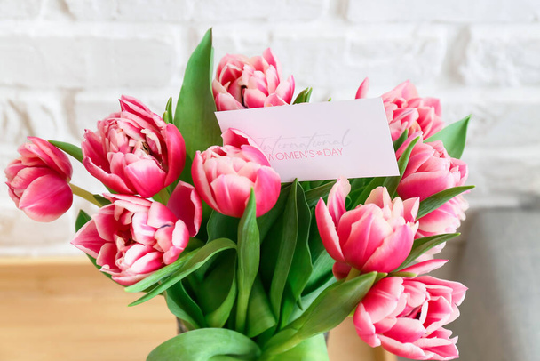 Bouquet of tulips and greeting card with text INTERNATIONAL WOMEN'S DAY, closeup - Photo, Image