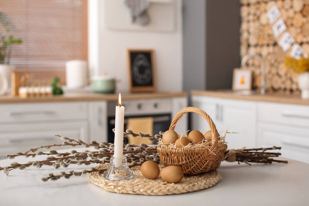 Basket with Easter eggs, pussy willow branches and burning candle on dining table - Foto, Bild