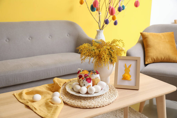 Piatto con torta pasquale, uova, cornice fotografica e fiori di mimosa sul tavolo di legno - Foto, immagini