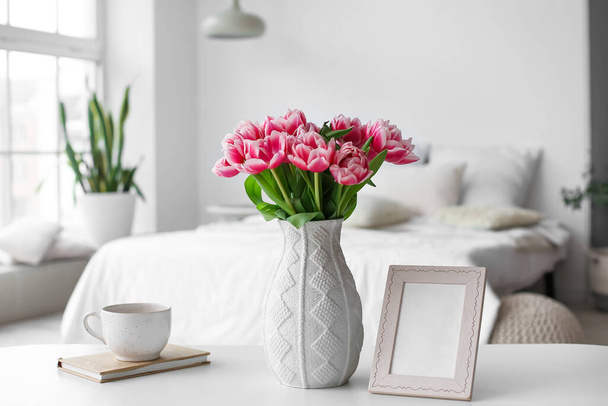 Vaas met tulpen, fotolijstje en beker op tafel in de kamer - Foto, afbeelding