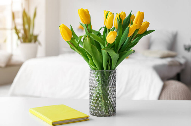 Vase with tulips and book on table in light room - Фото, зображення