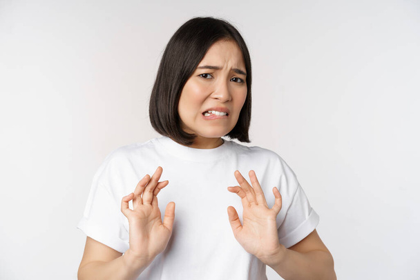 Disgusted asian woman rejecting smth, grimacing from dislike and aversion, stare with cringe, refusing offer, standing over white background - Photo, Image