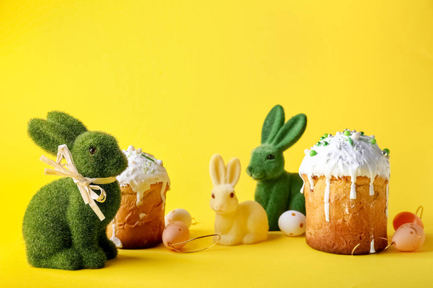 Cute Easter bunnies, cakes and painted eggs on yellow background - Photo, Image
