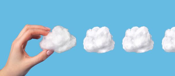 Banner with hand holding cotton cloud at blue background. Cloudy sky in surrealism style. Dreaming or weather concept  - Fotó, kép