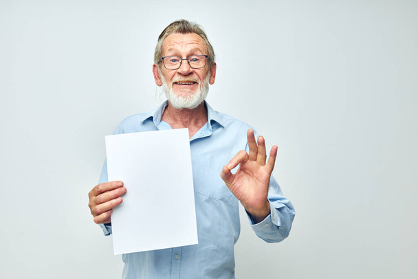 Senior grey-haired man blank sheet of paper gesture hands smile light background - Foto, Imagem