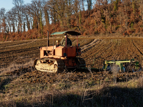 Mezőgazdaság, a mezőgazdasági munkák korai tavaszi időszakában vetés előtti tevékenységek részeként vetőmagtermesztővel ellátott földterületet előkészítő traktor. - Fotó, kép