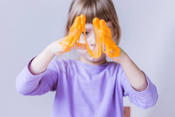 A girl in a lavender long sleeve stretches an orange slime with her hands - Valokuva, kuva