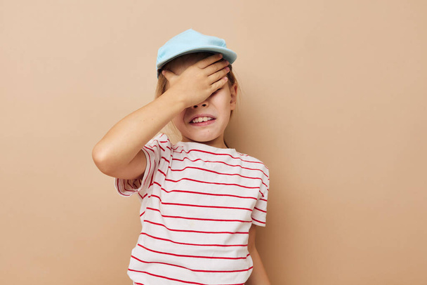 Portrait of happy smiling child girl in blue caps striped t-shirt emotions beige background - Photo, image