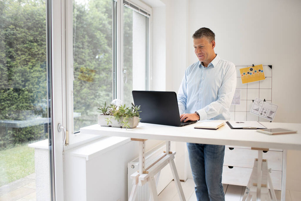 handsome businessman in blue shirt works at high table working on laptop - Fotografie, Obrázek