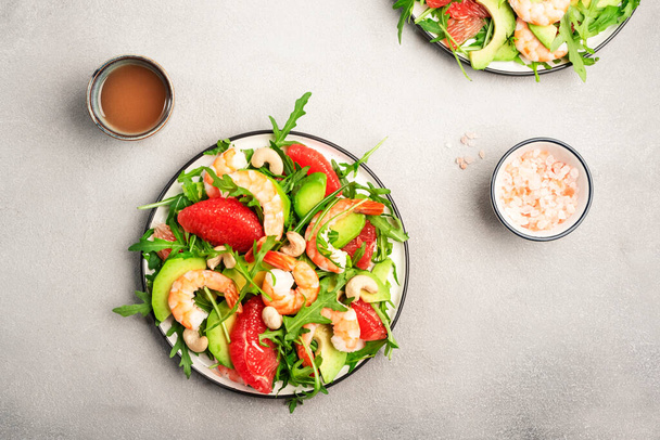 Delicious salad with shrimps, avocado, grapefruit, arugula and cashews. Grey stone table background, top view, negative space - Valokuva, kuva