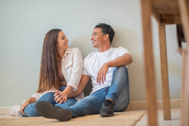 Gospodarka bankowości hipotecznej i kredytowej z młodą parą kupujących siedzi na podłodze w domu i uśmiech planowania do wyposażenia. Radosnych szczęśliwych ludzi w miłości i związku. Międzyrasowy chłopiec i dziewczyna - Zdjęcie, obraz