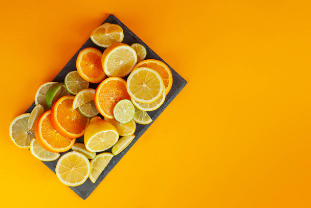 Oranges, lemons and limes cut into slices. Citrus vegetables on an orange background. Preparing vegetables for juice and cocktails. Copy space and free space for text near food. - Фото, зображення