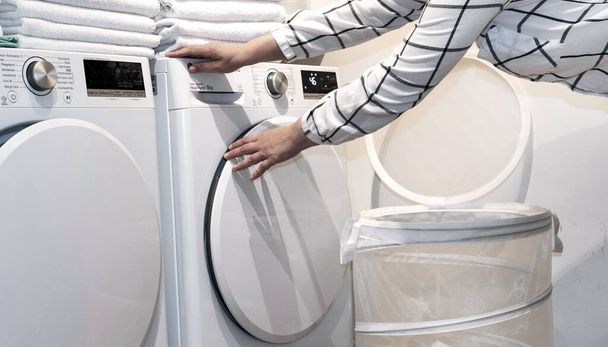 女性の手は洗濯機や乾燥機の近くにタオルを保持. - 写真・画像