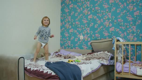 un pequeño niño feliz salta en la cama en casa y juega pelota con su padre, el padre le lanza la pelota fuera de la pantalla. - Metraje, vídeo