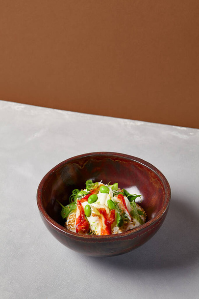 Chef salad with crab, quinoa, vegetables and edamame beans on dark homemade ceramic bowl. Salad bowl with crab, avocado, cream sauce in modern serveware. Modern dishware on concrete background - Foto, Imagen