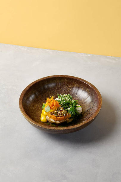 Pumpkin steak with chicken and spinach on dark ceramic plate. Healthy food in modern dishware. Innovative recipes in contemporary style. Roasted turkey with pumpkin on gray concrete background - 写真・画像