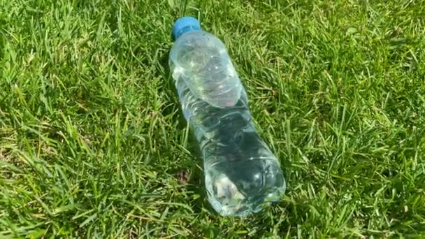 A bottle of fresh water laying on green grass outdoors in bright sunlight. Doing sport outdoors concept. Thirsty and water balance in hot weather concept. Bottle of water of transparent plastic. - Footage, Video