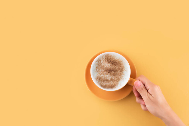 hand holding cup of cappuchino coffee on a yellow background. Space for text. - Photo, Image