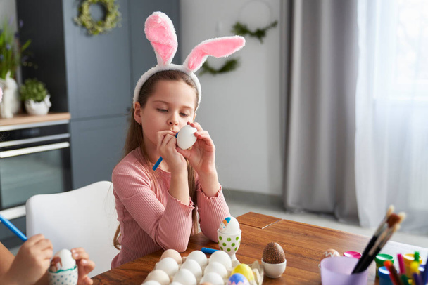 Kohdennettu valkoihoinen tyttö koristelu pääsiäismunia kotitalouskeittiössä  - Valokuva, kuva
