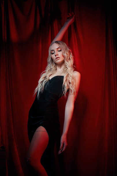 Beautiful blonde woman with long hair on a red velvet background. Hair jewelry on a woman head, modern makeup and arrows on the eyes - Valokuva, kuva