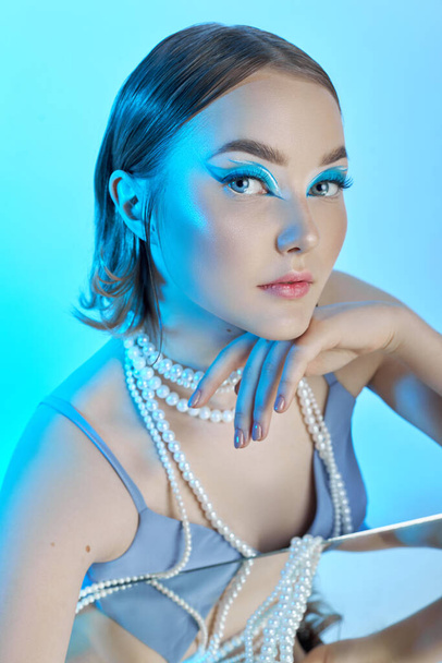Beauty portrait woman makeup blue arrows eyes, beads jewelry around her neck, blue dress, woman at table with milk. Art makeup Professional makeup and cosmetics face. Sophisticated art portrait style - Foto, imagen