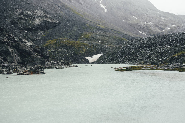 Bleak rainy landscape with rain circles on water surface of mountain lake. Atmospheric mountain scenery with mountain lake among moraines in rainy weather. Beautiful gloomy view to glacier lake. - Photo, Image