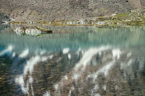 Rock in turquoise bergmeer. Snowy berg weerspiegeld in azuurhelder water van gletsjermeer. Mooie zonnige achtergrond met sneeuwwitte gletsjer reflectie in groen water oppervlak van bergmeer. - Foto, afbeelding