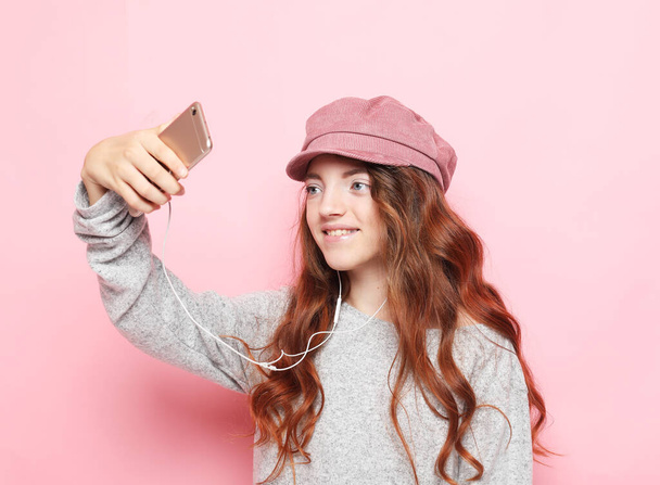 Portrait of a cheerful little girl wearing hat taking a selfie isolated over pink background. Lifestyle and childhood concept. - Φωτογραφία, εικόνα