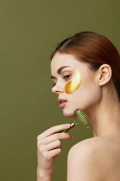 beautiful woman jade roller golden patches clean skin smile posing green background - Fotografie, Obrázek