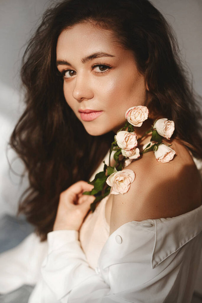 A young caucasian model woman with gentle makeup posing with branch of flowers over white background. Model girl with branch of roses - Fotó, kép