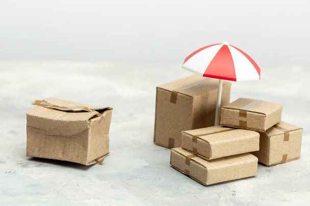 Poštovní pojištění. Zmačkaná a rozbitá krabička s kartónovými krabicemi chráněnými deštníkem - Fotografie, Obrázek