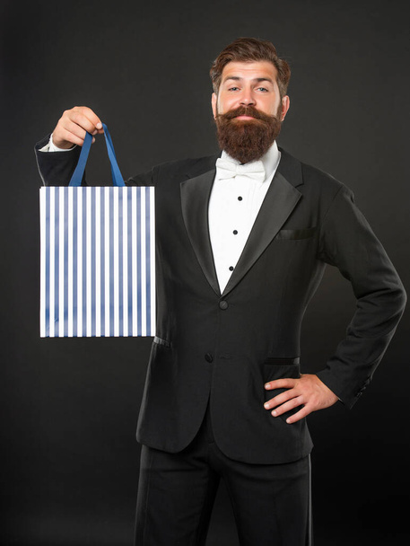 smiling man in tuxedo bow tie formalwear on black background with purchase shopping bag. copy space - Fotoğraf, Görsel