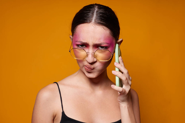 fashionable woman with phone pink face makeup posing attractive look glasses yellow background unaltered - Photo, Image