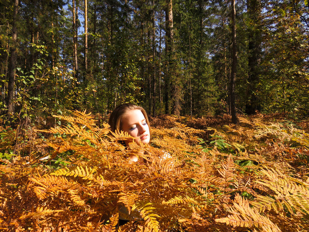 Young blonde woman with bare shoulders in a thicket of yellow ferns in an autumn forest - Foto, imagen