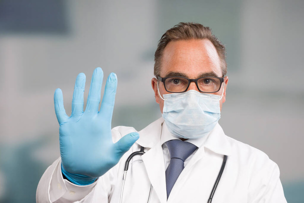 άνδρας γιατρός φορώντας μια ιατρική μάσκα προσώπου και ιατρικά γάντια κάνει μια χειρονομία στάση - Φωτογραφία, εικόνα