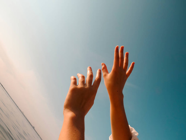 Hands of a young woman pointing to the sky in the sunlight on a summer evening at sunset, tilted horizon, close-up, the concept of outdoor recreation, harmony, peace, unity, love with the surrounding world - Valokuva, kuva