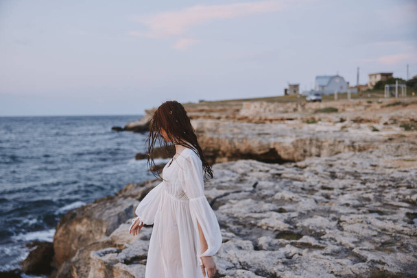 eine Frau geht in einem weißen Kleid auf den Felsen am Meer - Foto, Bild