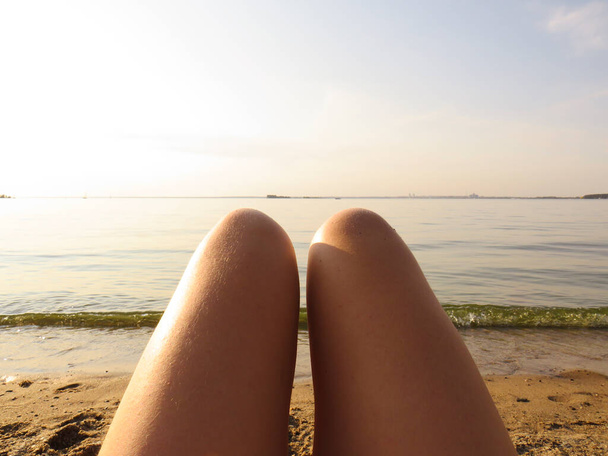 Tanned slender legs of a young woman on a sandy beach on the background of the water of the sea bay at sunset, the concept of beauty and health of the female body, beach holidays, healthy lifestyle, outdoor activities - Zdjęcie, obraz