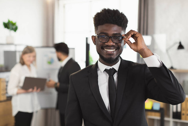 Smiling african man in suit and eyeglasses posing at office - Fotó, kép