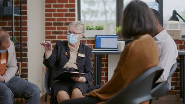 Κοντινό πλάνο της ψυχιάτρου γυναίκα μιλάει με τους ανθρώπους σε μια ομαδική θεραπεία, φορώντας μάσκα προσώπου - Φωτογραφία, εικόνα