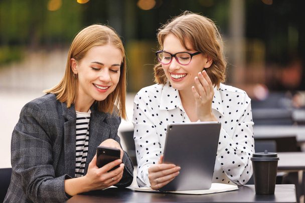 Innoissaan menestyviä liiketoiminnan naisia ulkona kahvila tarkastellaan digitaalinen tabletti ja älypuhelin onnellinen ilme - Valokuva, kuva