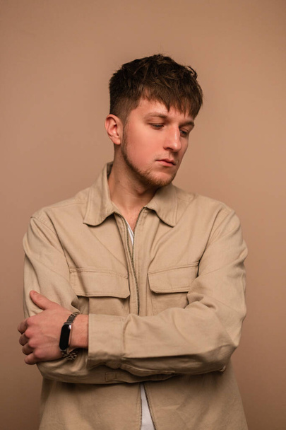 Cool young stylish man with a hairstyle in fashionable outerwear on a beige background - 写真・画像