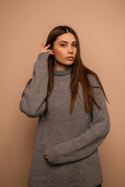 Young pretty girl with natural beauty in a fashionable knitted sweater stands near beige background in the studio. Portrait of woman - Foto, afbeelding