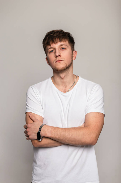 Stylish handsome hipster man with hairstyle in white fashion mockup t-shirt poses in studio - Fotó, kép