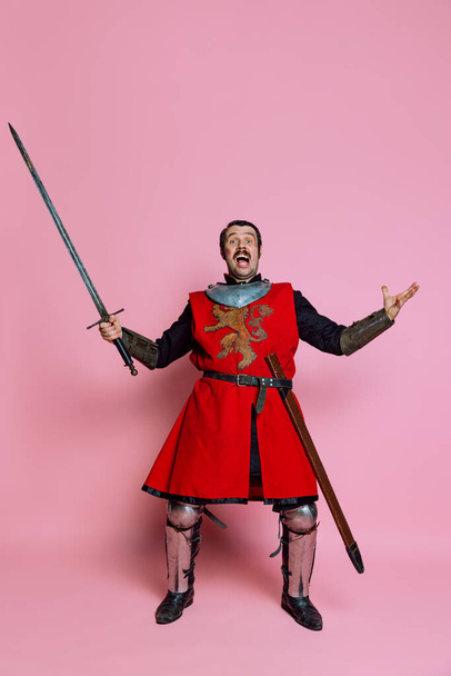 One young man, medieval warrior or knight wearing wearing armor clothing posing isolated over pink background. Comparison of eras, history, wow emotions - Φωτογραφία, εικόνα